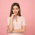 Portrait of a young woman posing elegantly in a studio with a pink background.