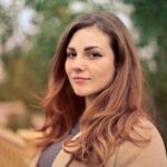 A young woman with long hair smiles confidently for an outdoor portrait session.